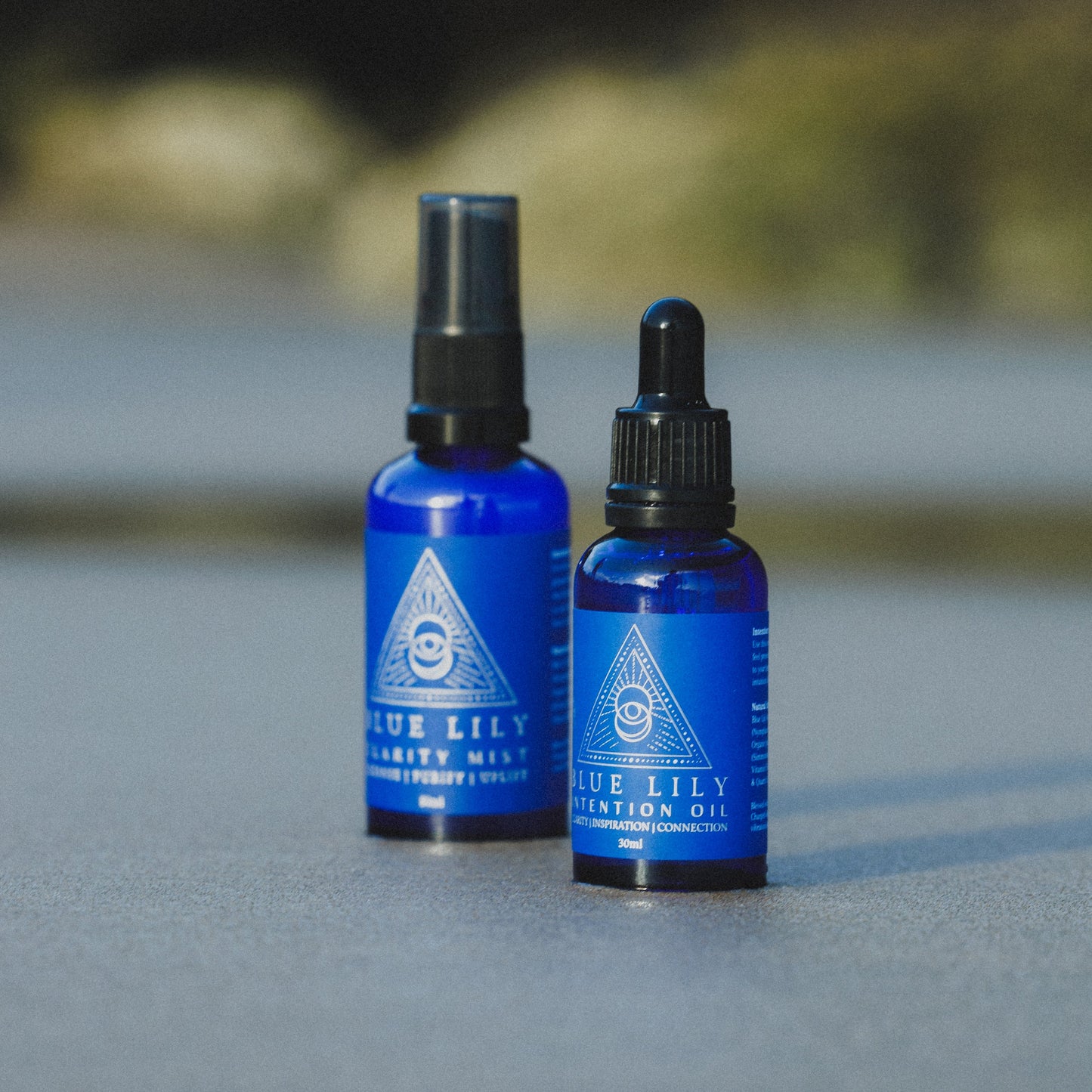 two glass blue bottle standing on the sand called clarity mist and intention oil