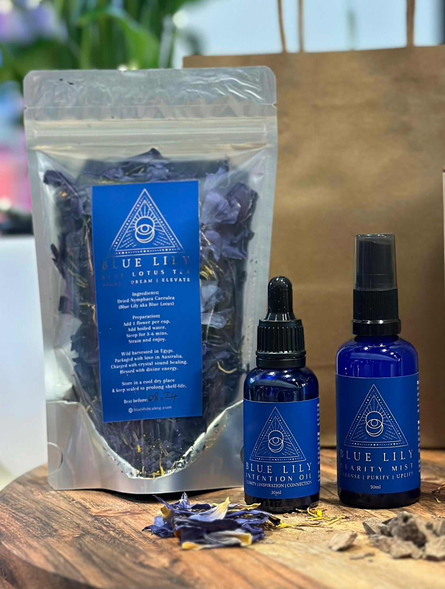 A set of self-care products including a pouch of Blue lotus essential oil and spray bottle, all with labels and displayed on a wooden surface.